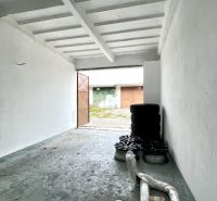 V garáži jsou pneumatiky a ráfky, betonová podlaha, studené bílé stěny.