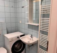 Koupelna v 1-pokojovém bytě s pračkou a umyvadlem, světle modré obklady.