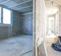 Interiér rozestavěného rodinného domu s betonovými stěnami a velkými okny.