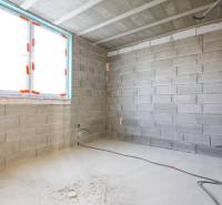 Interiér s nedokončenými stěnami, instalací elektrických kabelů a oknem v rodinném domě.