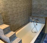 Koupelna s litinovou vanou a schůdky, typická pro 2-pokojový byt.