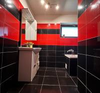 Černo-červená koupelna v rodinném domě se zrcadlem a vanou, výrazná kombinace obkladů.