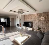 Obývací pokoj v rodinném domě s pohovkou, TV a krbem, podlaha s dřevěným dekorem.