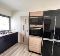 Kuchyně v rodinném domě s plynovým sporákem a spotřebiči, podlaha s dřevěným dekorem.