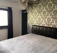 Ložnice v rodinném domě s dekorativní tapetou a lustrem. Symfonie interiérového designu.