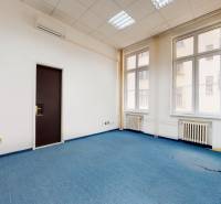 Kanceláře s modrým kobercem, bílými stěnami a velkými okny.