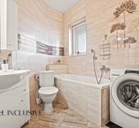 Koupelna v 2-pokojovém bytě s pračkou, vanou, umyvadlem a obloženými stěnami.