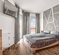 Ložnice v 2-pokojovém bytě s televizí, postelí a podlahou s dřevěným dekorem.