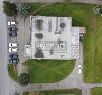 Pohled shora na obchodní prostory v Rimavské Sobotě, obklopené zelení a zaparkovanými auty.