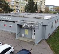 Budova obchodního prostoru v Rimavské Sobotě, obklopená paneláky a zaparkovanými auty.