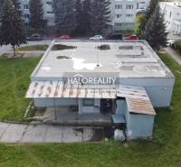 Pohled na obchodní prostory v Rimavské Sobotě s přilehlým parkem a betonovou střechou.