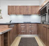 Kuchyně v 2-pokojovém bytě s dřevěnými skříňkami, bílým obkladem a podlahou s dřevěným dekorem.