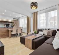 Obývací pokoj s podlahou s dřevěným dekorem v 2pokojovém bytě s rohovou sedačkou a kuchyní.