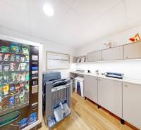 Kanceláře s automatem na občerstvení, tiskárnou a skříněmi, podlaha s dřevěným dekorem.