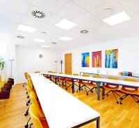 Interiér kanceláře s podlahou s dřevěným dekorem, žluté židle a moderní umělecké obrazy.