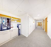 Kancelář s kávovarem a vodním automatem, světlé stěny a koberec.