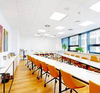 Kancelář s bílými stoly, oranžovými židlemi a podlahou s dřevěným dekorem.