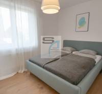 Ložnice s velkou postelí, záclonami a podlahou s dřevěným dekorem v 2-pokojovém bytě.