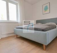 Ložnice v 2-pokojovém bytě, světlá postel, podlaha s dřevěným dekorem, jednoduchý dekor.