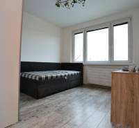 Pokoj v 3-pokojovém bytě, podlaha s dřevěným dekorem, gauč a komoda.