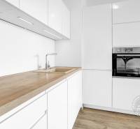 Kuchyňská linka s dřevěným dekorem, bílé skříňky a vestavná trouba v 2-pokojovém bytě.