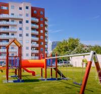 Bytový dům na Bosákově ulici v Bratislavě - Petržalce s dětským hřištěm na trávníku.
