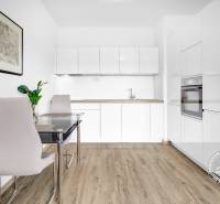 Kuchyně v 2-pokojovém bytě s bílou linkou, jídelním stolem a podlahou s dřevěným dekorem.