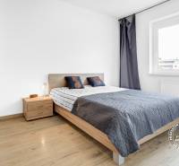 Ložnice s šedým přehozem, dřevěnou skříní a podlahou s dřevěným dekorem v dvoupokojovém bytě.