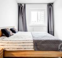 Ložnice s postelí, nočním stolkem a oknem v dvoupokojovém bytě.