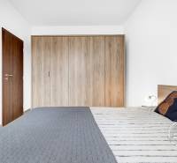 Ložnice v 2pokojovém bytě se skříní a manželskou postelí s podlahou s dřevěným dekorem.