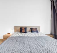 Světlá ložnice s postelí, šatní skříní a podlahou s dřevěným dekorem v 2pokojovém bytě.