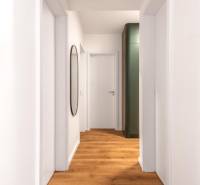 Úzký interiér s podlahou s dřevěným dekorem a jednoduchou bílou stěnou v 3-pokojovém bytě.