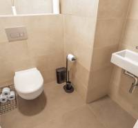 Toaleta se závěsnou mísou v 3-pokojovém bytě, béžové obklady, malé umyvadlo.