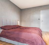 Ložnice s postelí ve 3pokojovém bytě, šedé stěny, podlaha s dřevěným dekorem.