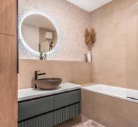 Koupelna v 3-pokojovém bytě se vzorovanou stěnou, kulatým zrcadlem a vanou.