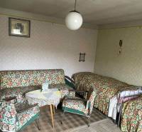 Pokoj v rodinném domě s retro nábytkem, vzorovanými potahy a kobercem.