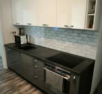 Kuchyně ve 3-pokojovém bytě s tmavými skříňkami a podlahou s dřevěným dekorem.