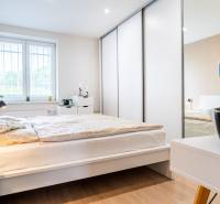 Ložnice v 3-pokojovém bytě s podlahou s dřevěným dekorem a bílým nábytkem.