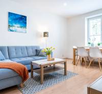 Obývací pokoj v 3-pokojovém bytě s pohovkou a jídelním stolem, podlaha s dřevěným dekorem.