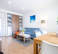 Obývací pokoj v 3-pokojovém bytě s modrou sedačkou a podlahou s dřevěným dekorem.