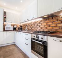 Kuchyně ve 3-pokojovém bytě, s cihlovou stěnou a moderními spotřebiči.