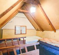 Podkrovní pokoj v chatě se střešními trámy a jednoduchým nábytkem.