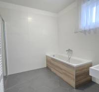 Koupelna v rodinném domě s vanou s dřevěným dekorem a bílými obkladačkami.