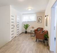 Interiér rodinného domu s podlahou s dřevěným dekorem, pohodlnými křesly a rostlinami.