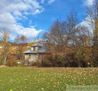 Rodinný dům v Liptovských Beharovcích obklopený podzimními stromy a zelenou loukou.