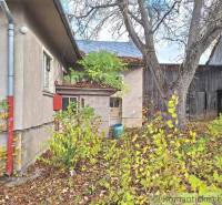 Na dvoře rodinného domu v Liptovských Beharovcích jsou vidět stromy a dřevěné stavby.