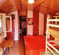 Interiér chaty s poschoďovou postelí, podlahou s dřevěným dekorem a otevřeným oknem.