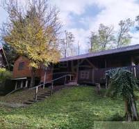 Chata v Dudincích obklopená přírodou s terasou a stromy na dvoře.