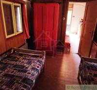 Interiér chaty s dvěma lůžky, červenou skříní a kobercem s geometrickým vzorem.