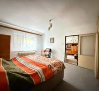 Ložnice v rodinném domě se světlým kobercem, oknem a postelí s dekou.